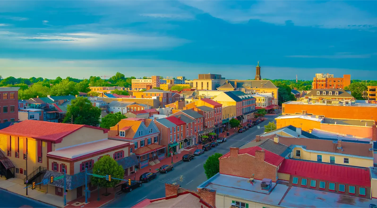 Aerial view of a small town street with cars parked along colorful historic buildings under a clear sky.